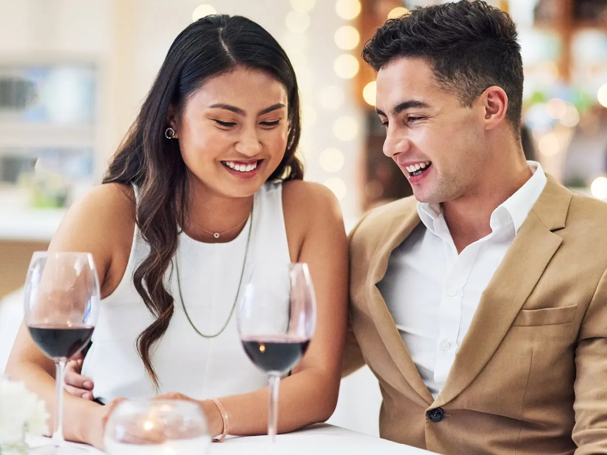 A finely dressed woman and man seated at a table drinking wine